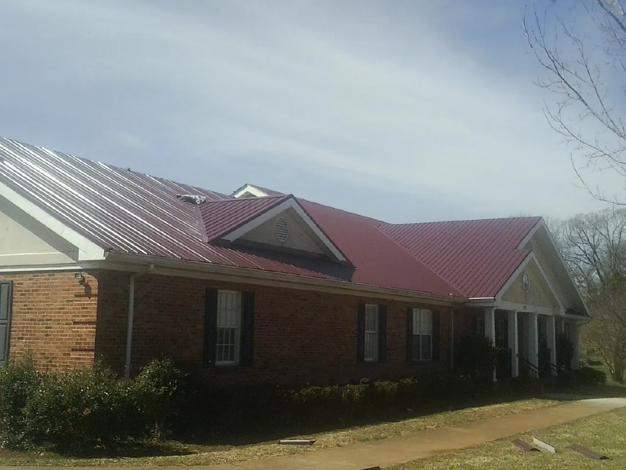 Red metal roof with gabled entries on a long brick building, from a Hail Damage Roof Repair job in Richmond Hill