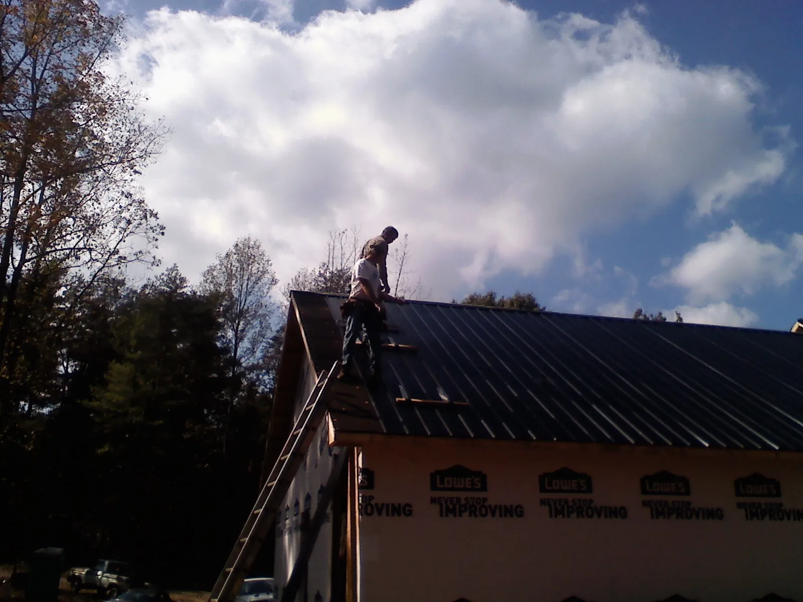 Roofer fastening dark metal panels high against a cloudy sky, from a Roof Inspection job in Richmond Hill