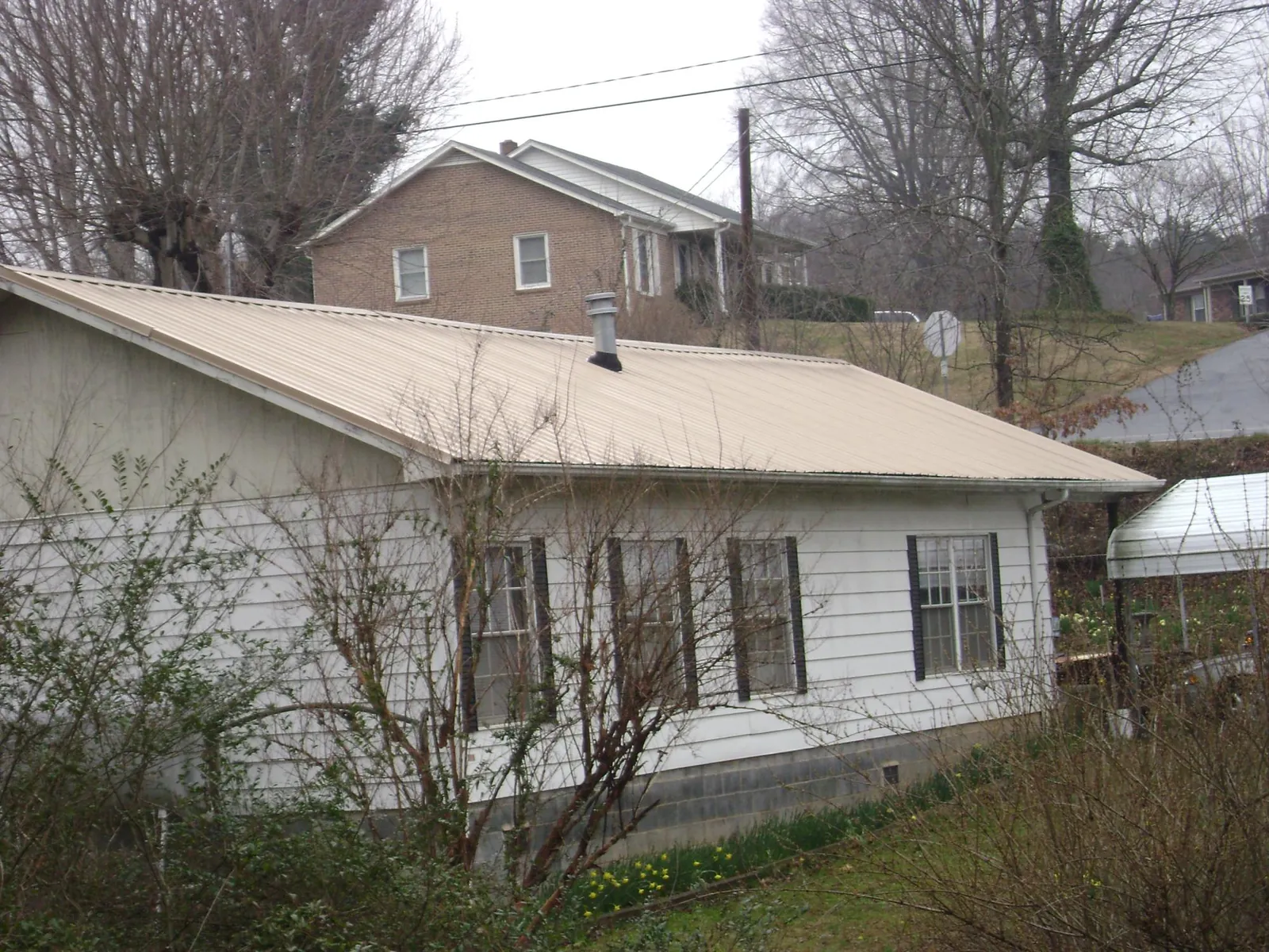 Tan metal roof on a white sided house set into a hillside — Commercial Roofing by Roofing Brothers in Richmond Hill